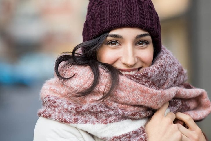 Closeup face of a young happy woman enjoying winter wearing scarf and cap. Smiling girl in a colorful shawl looking at camera. Latin woman with knitted bordeaux hat and woolen scarf.