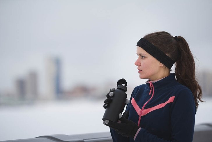 Young woman jogging outside cloudy winter day - drink water